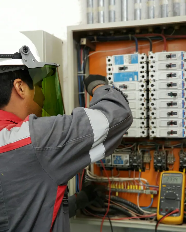 Koruyucu siperlikle dağıtım panosunda kablo bağlayan elektrik teknisyeni